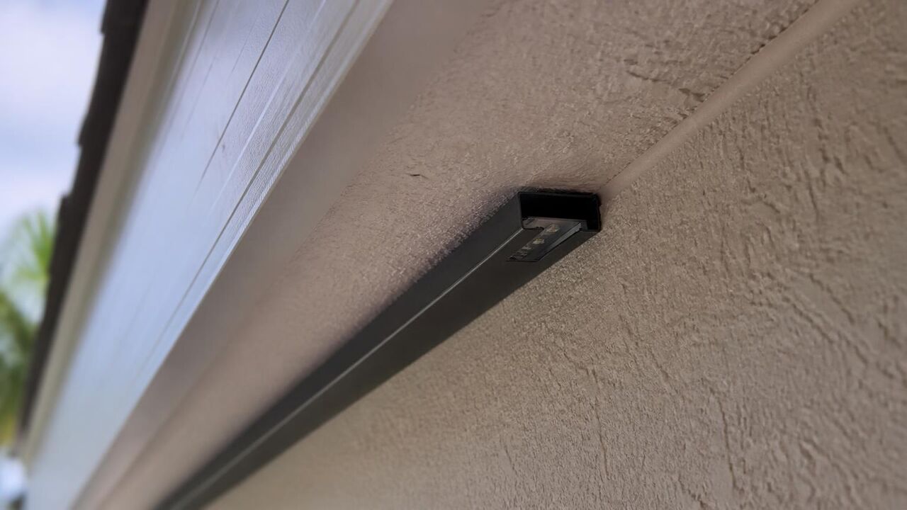 Close-up of a slim black aluminum channel with hidden LED modules mounted under the soffit of a Lathrop house