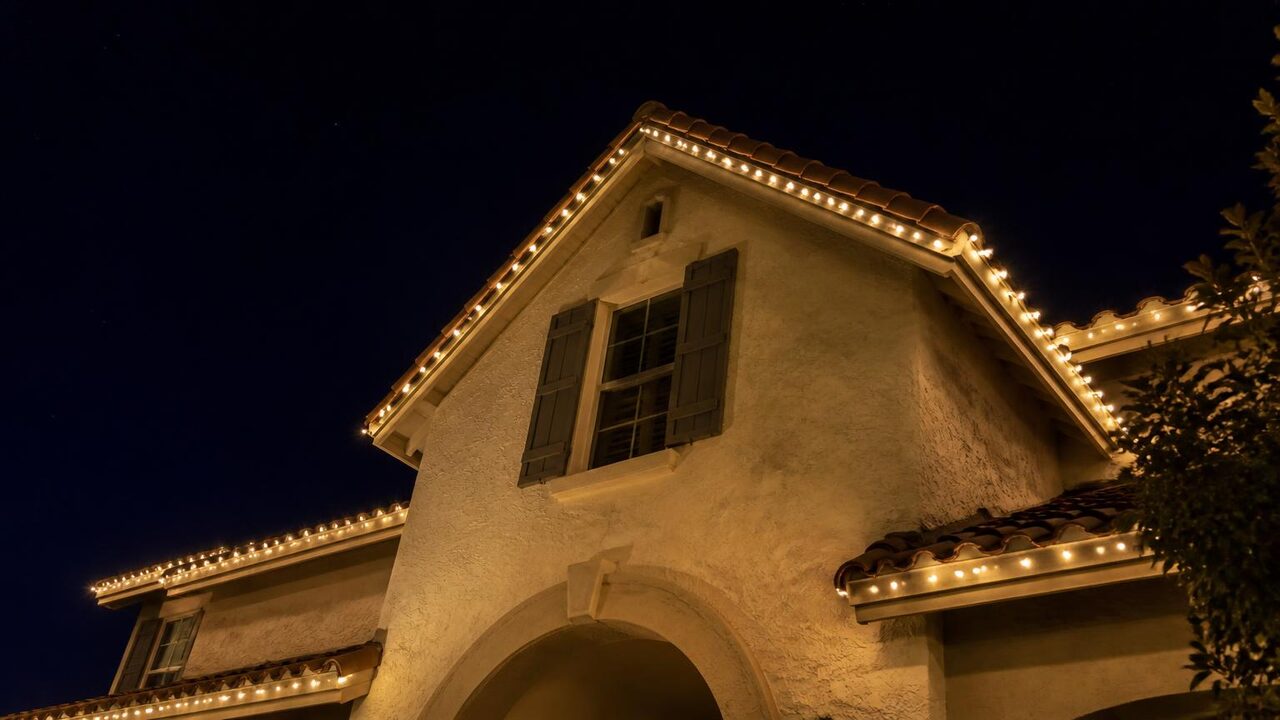 Upward view of a steep two-story gable peak on a Manteca stucco home outlined in warm white permanent LED points