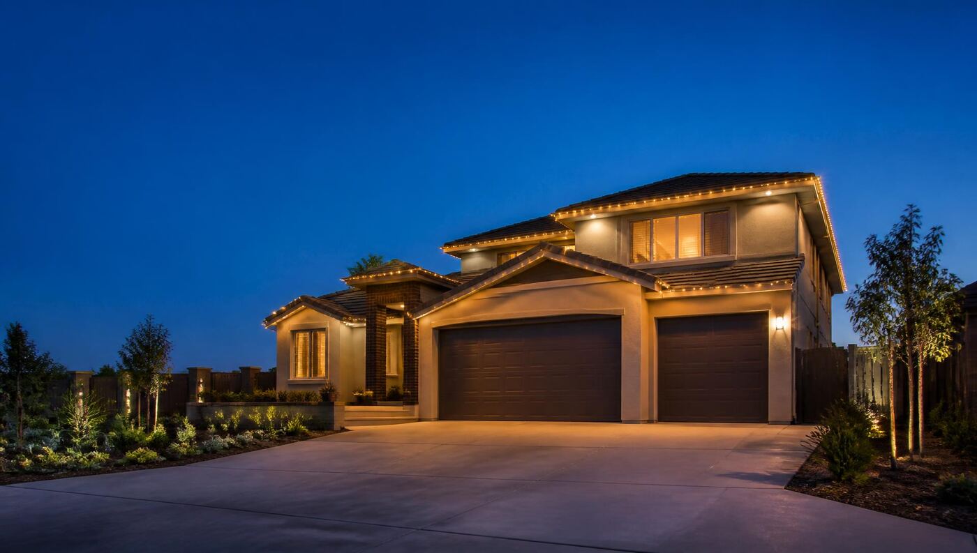 Warm white permanent holiday lighting installed along the rooflines and gable peaks of a two-story Manteca home at dusk